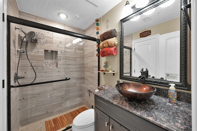 bathroom with vanity, toilet, a textured ceiling, and a shower with door