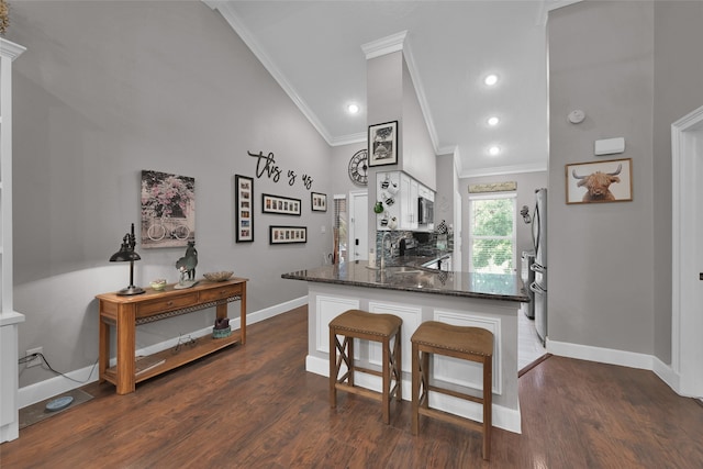 kitchen with white cabinets, crown molding, dark hardwood / wood-style flooring, kitchen peninsula, and high vaulted ceiling