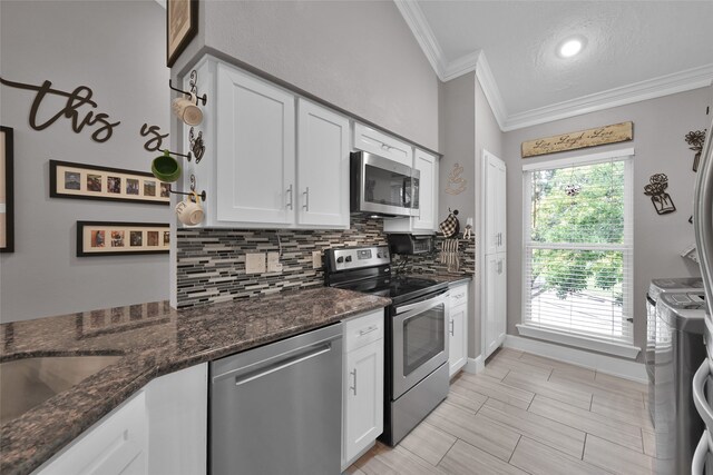 kitchen featuring appliances with stainless steel finishes, dark stone counters, white cabinetry, and ornamental molding