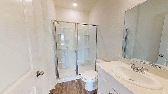 bathroom featuring hardwood / wood-style floors, walk in shower, toilet, and vanity