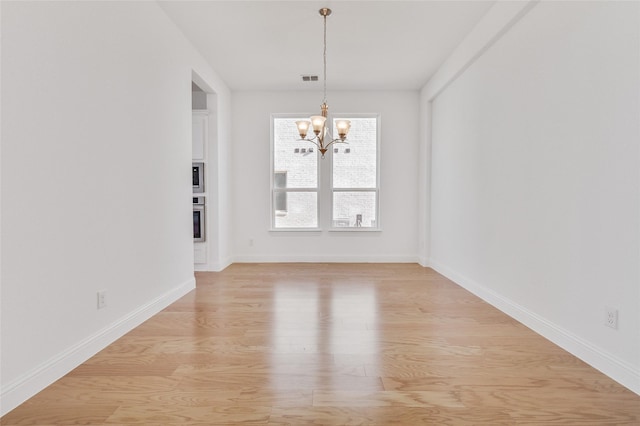 unfurnished dining area featuring visible vents, baseboards, light wood-type flooring, and an inviting chandelier