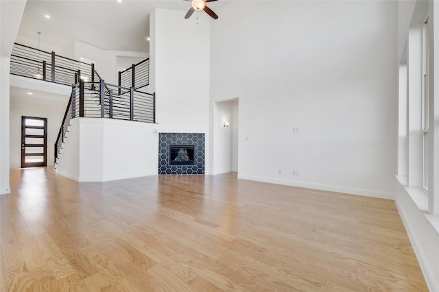 unfurnished living room featuring a ceiling fan, wood finished floors, a high ceiling, a fireplace, and stairs