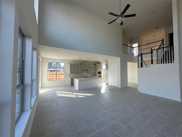 unfurnished living room with a high ceiling, baseboards, visible vents, and a sink