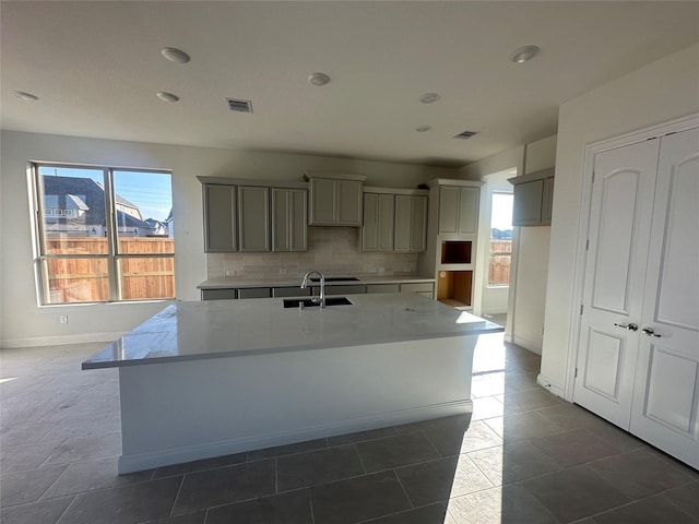 kitchen with tasteful backsplash, a healthy amount of sunlight, gray cabinetry, a center island with sink, and a sink