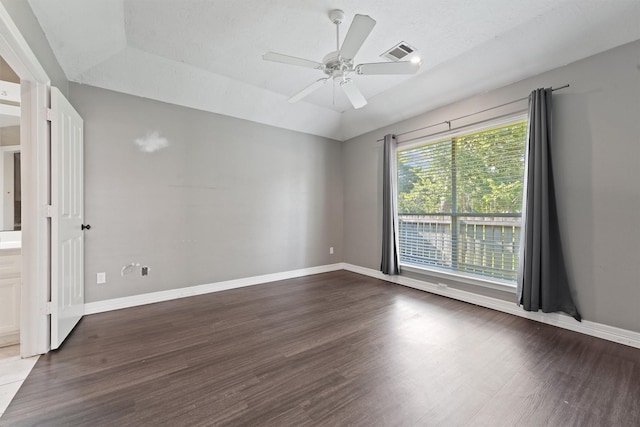 spare room featuring a ceiling fan, baseboards, visible vents, dark wood-type flooring, and vaulted ceiling