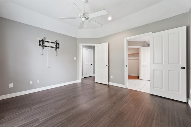 unfurnished bedroom featuring wood finished floors, a closet, baseboards, ceiling fan, and a spacious closet