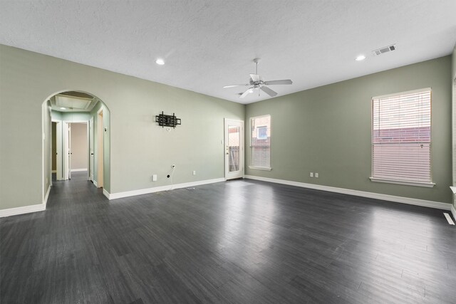 empty room with a ceiling fan, visible vents, baseboards, dark wood finished floors, and arched walkways