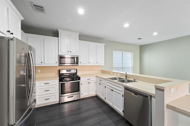 kitchen featuring visible vents, a peninsula, a sink, dark wood-type flooring, and appliances with stainless steel finishes