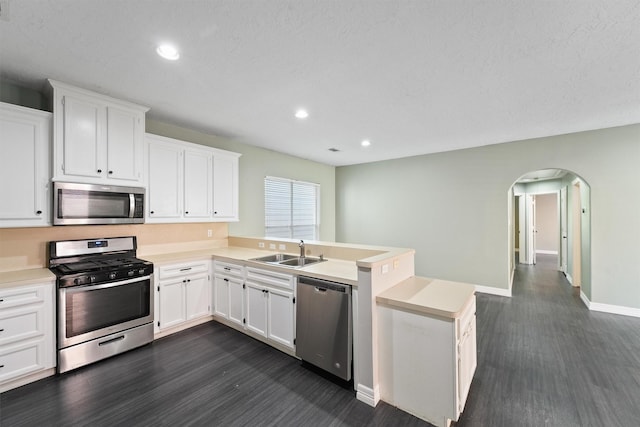 kitchen featuring light countertops, a peninsula, arched walkways, stainless steel appliances, and a sink