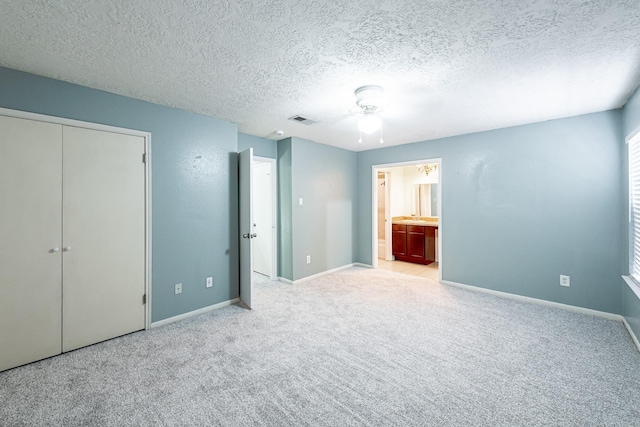 unfurnished bedroom featuring ensuite bathroom, light colored carpet, ceiling fan, a textured ceiling, and a closet