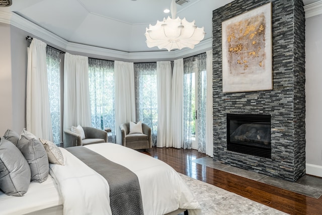 bedroom featuring an inviting chandelier, a fireplace, a tray ceiling, dark wood-type flooring, and ornamental molding