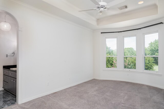 carpeted empty room with ceiling fan, a wealth of natural light, a raised ceiling, and ornamental molding