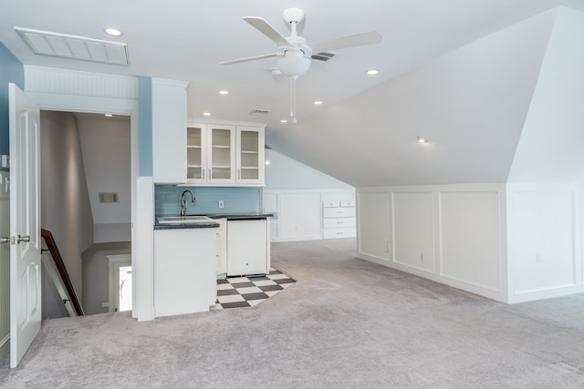 kitchen with light carpet, white dishwasher, ceiling fan, vaulted ceiling, and white cabinets