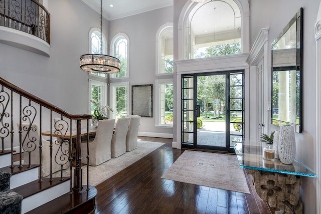 entrance foyer with dark wood-type flooring, a wealth of natural light, a notable chandelier, and a towering ceiling