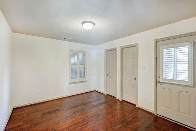 unfurnished bedroom featuring a textured ceiling, multiple windows, and dark hardwood / wood-style flooring