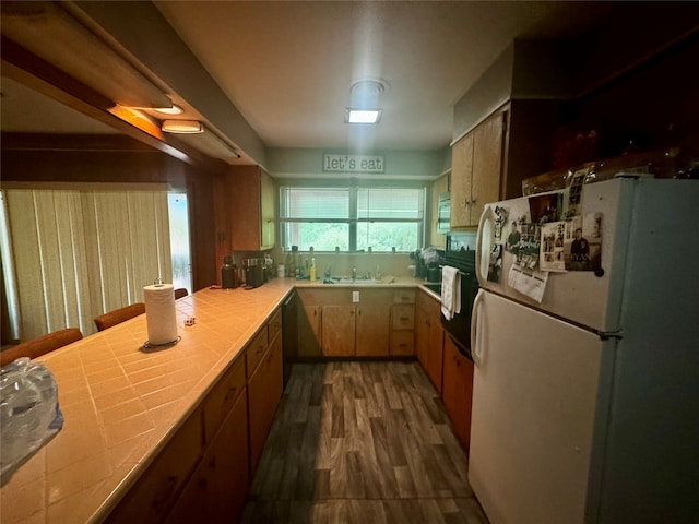 kitchen with tile counters, black appliances, sink, and dark wood-type flooring