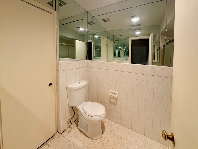 bathroom featuring tile walls, toilet, and a shower with door