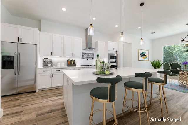 kitchen with stainless steel appliances, white cabinetry, a kitchen island with sink, and wall chimney range hood