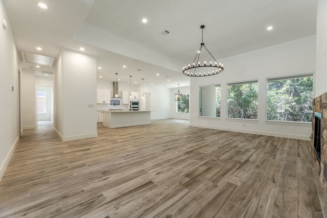 unfurnished living room with plenty of natural light, light hardwood / wood-style floors, a stone fireplace, and a chandelier