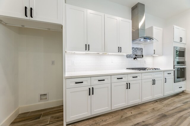 kitchen with white cabinets, wall chimney exhaust hood, appliances with stainless steel finishes, and tasteful backsplash