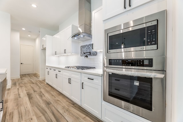 kitchen featuring light hardwood / wood-style floors, white cabinetry, stainless steel gas stovetop, and wall chimney range hood