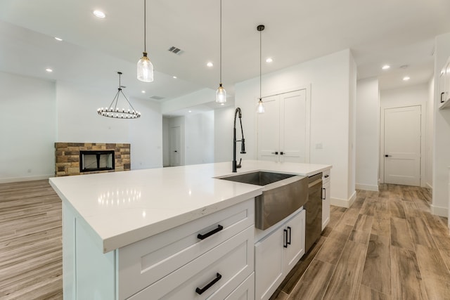 kitchen featuring white cabinetry, dishwasher, decorative light fixtures, a kitchen island with sink, and a fireplace