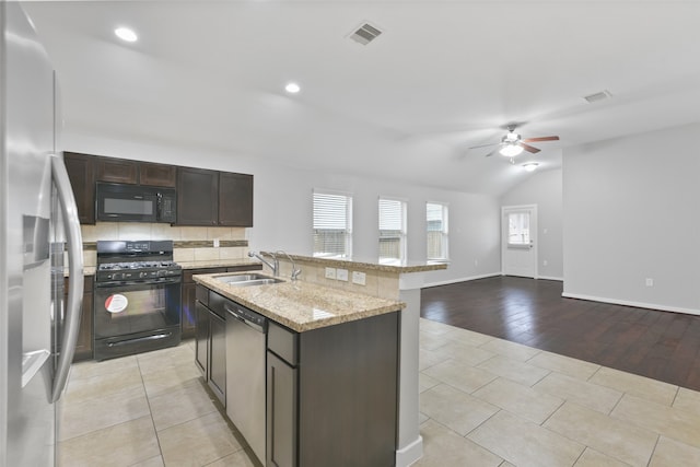 kitchen featuring light wood-type flooring, sink, black appliances, ceiling fan, and a center island with sink