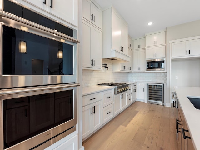 kitchen featuring beverage cooler, decorative backsplash, appliances with stainless steel finishes, white cabinets, and light hardwood / wood-style floors