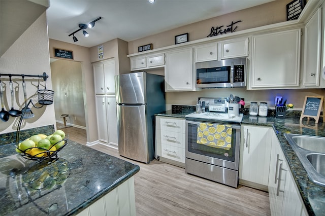 kitchen with appliances with stainless steel finishes, rail lighting, white cabinetry, and light hardwood / wood-style flooring