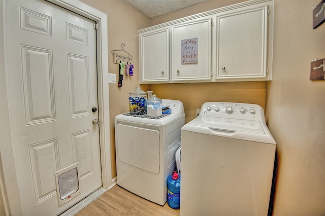 clothes washing area featuring light wood-type flooring, a textured ceiling, separate washer and dryer, and cabinets