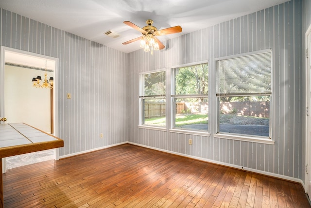 empty room featuring hardwood / wood-style flooring and ceiling fan with notable chandelier