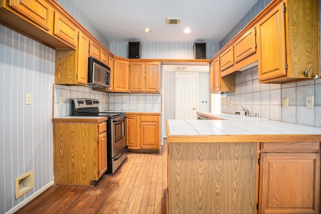 kitchen with dark wood-type flooring, electric range, tasteful backsplash, tile counters, and kitchen peninsula