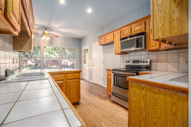 kitchen with appliances with stainless steel finishes, tasteful backsplash, ceiling fan, sink, and tile counters