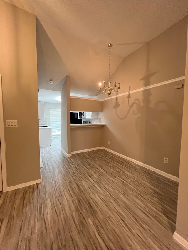 unfurnished living room with a textured ceiling, vaulted ceiling, a notable chandelier, and wood-type flooring