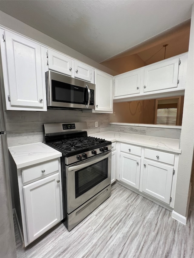 kitchen with stainless steel appliances, white cabinetry, and light hardwood / wood-style floors