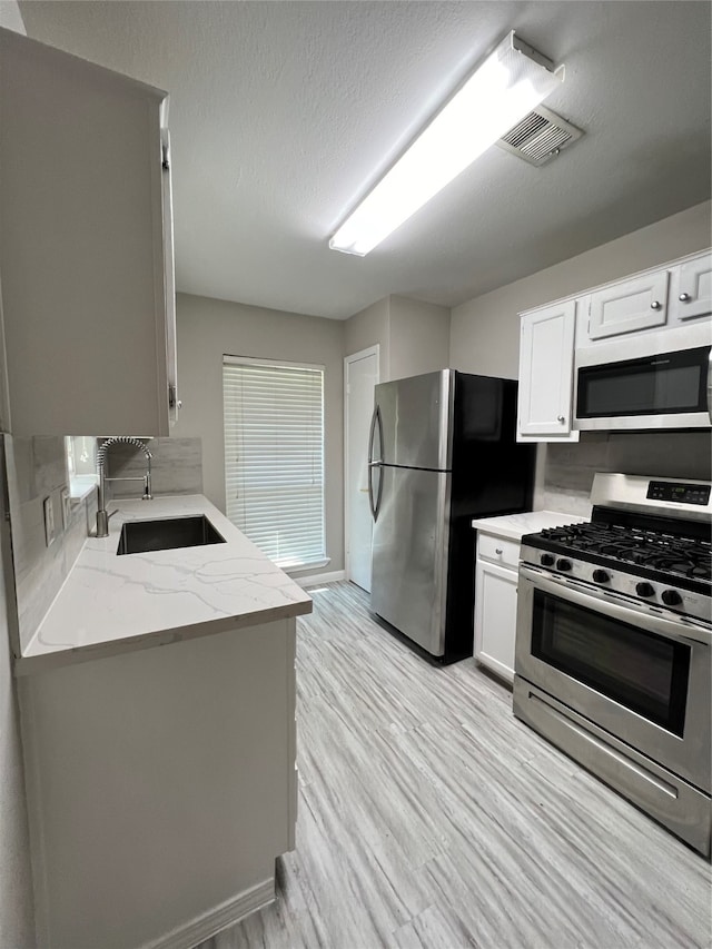 kitchen featuring white cabinets, appliances with stainless steel finishes, sink, and light hardwood / wood-style flooring