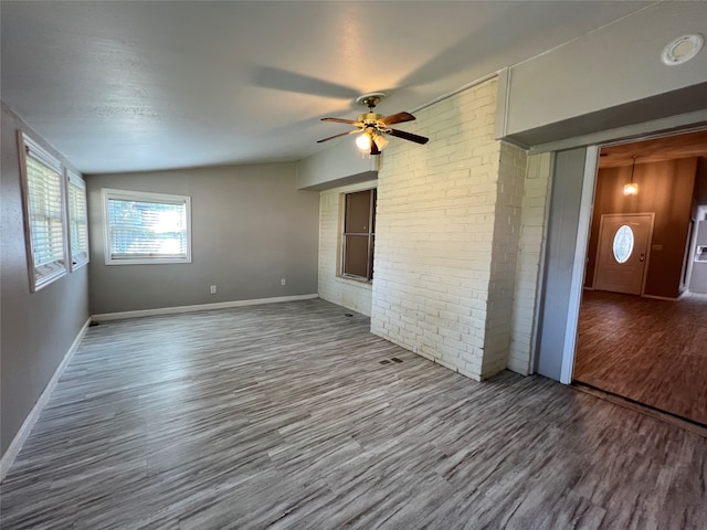 unfurnished room with vaulted ceiling, hardwood / wood-style flooring, brick wall, and ceiling fan