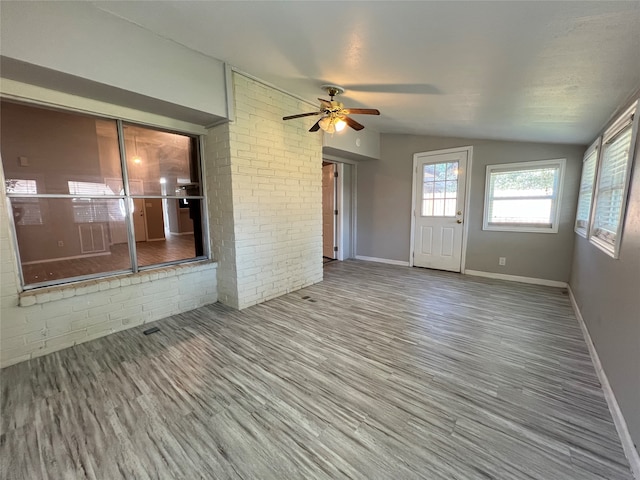 empty room featuring lofted ceiling, hardwood / wood-style floors, ceiling fan, and brick wall