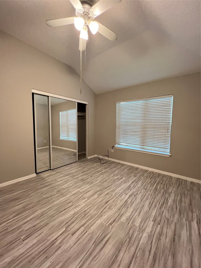 unfurnished bedroom with a textured ceiling, vaulted ceiling, a closet, light hardwood / wood-style floors, and ceiling fan