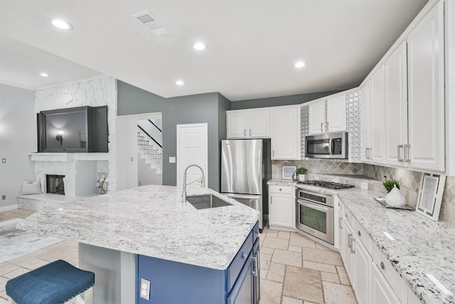 kitchen with an island with sink, stainless steel appliances, blue cabinets, white cabinets, and sink