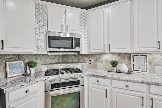 kitchen with decorative backsplash, light stone countertops, stainless steel appliances, and white cabinetry