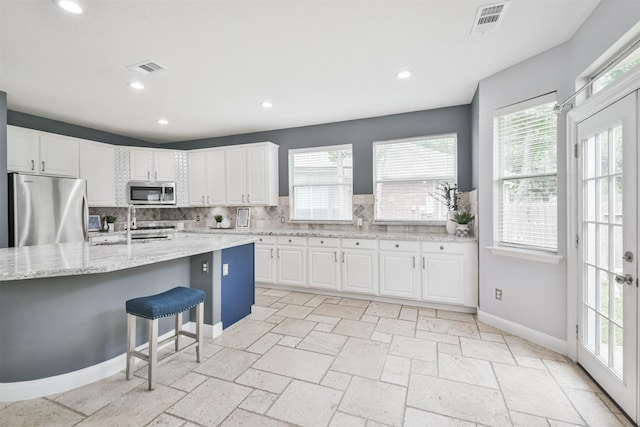 kitchen with backsplash, a center island with sink, appliances with stainless steel finishes, a kitchen breakfast bar, and white cabinets