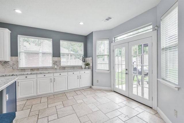 kitchen with light stone counters, white cabinets, french doors, and tasteful backsplash