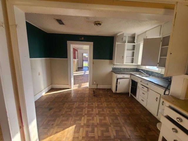 kitchen with white cabinets, dark parquet flooring, sink, and a textured ceiling