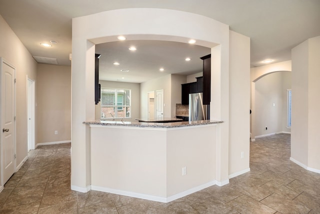 kitchen featuring light stone countertops, kitchen peninsula, and stainless steel refrigerator