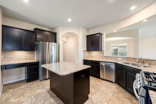 kitchen featuring backsplash, light stone counters, sink, a kitchen island, and appliances with stainless steel finishes