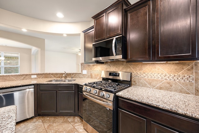 kitchen with appliances with stainless steel finishes, dark brown cabinets, light stone counters, and sink