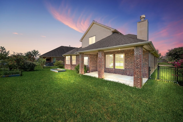 back house at dusk featuring a lawn and a patio