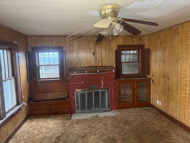 unfurnished living room featuring wood walls, ceiling fan, and carpet floors