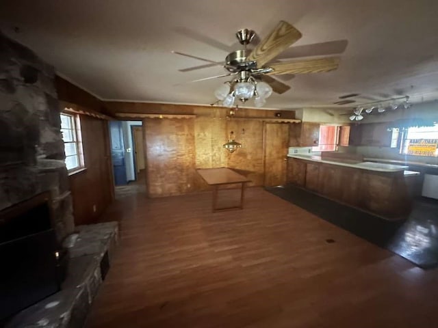 kitchen featuring hardwood / wood-style floors, ceiling fan, wood walls, and a stone fireplace